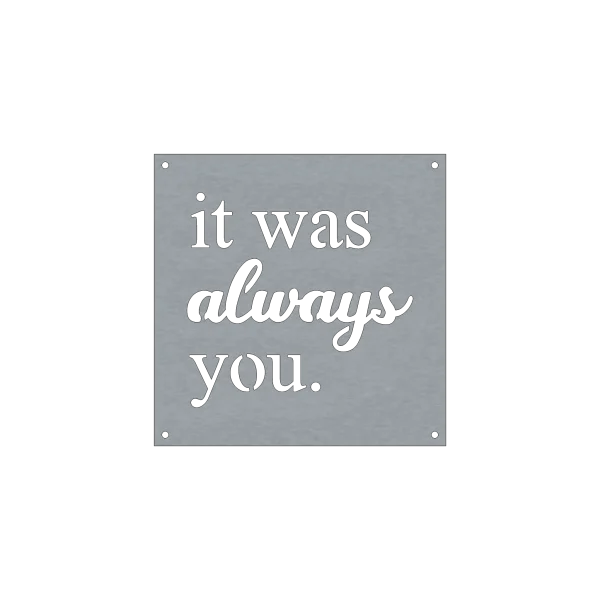 A square steel sign with precision-cut lettering spelling 'it was always you.' The words 'always' are in a cursive script, while the rest are in a simple, sans-serif font. The background is a smooth metallic grey with four small holes at each corner for mounting. The design is minimalist, emphasizing the contrast between the black lettering and the metal background.